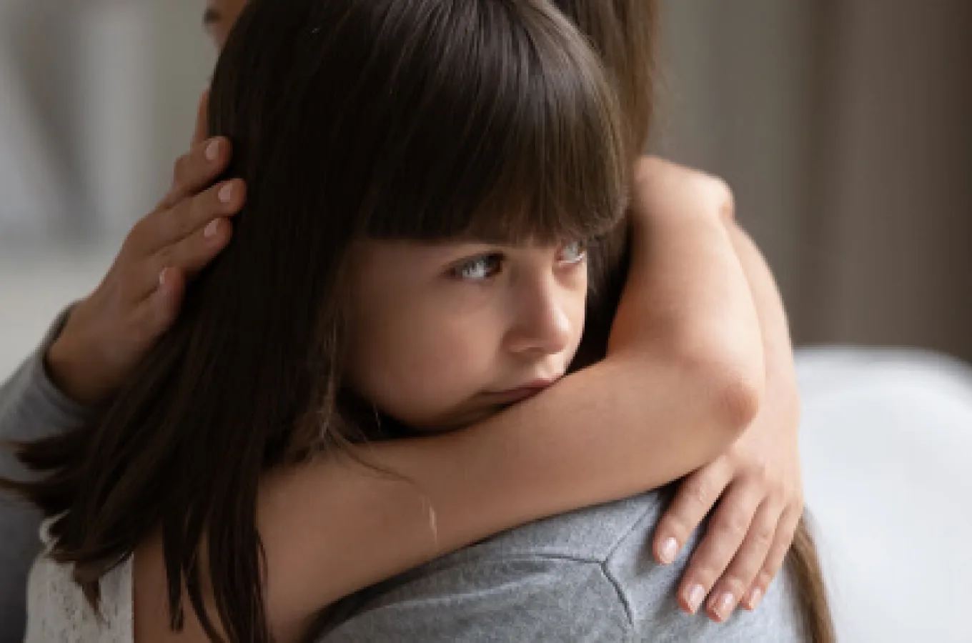 A child hugging an adult, chin resting on the adult's shoulder and eyes looking off to the side