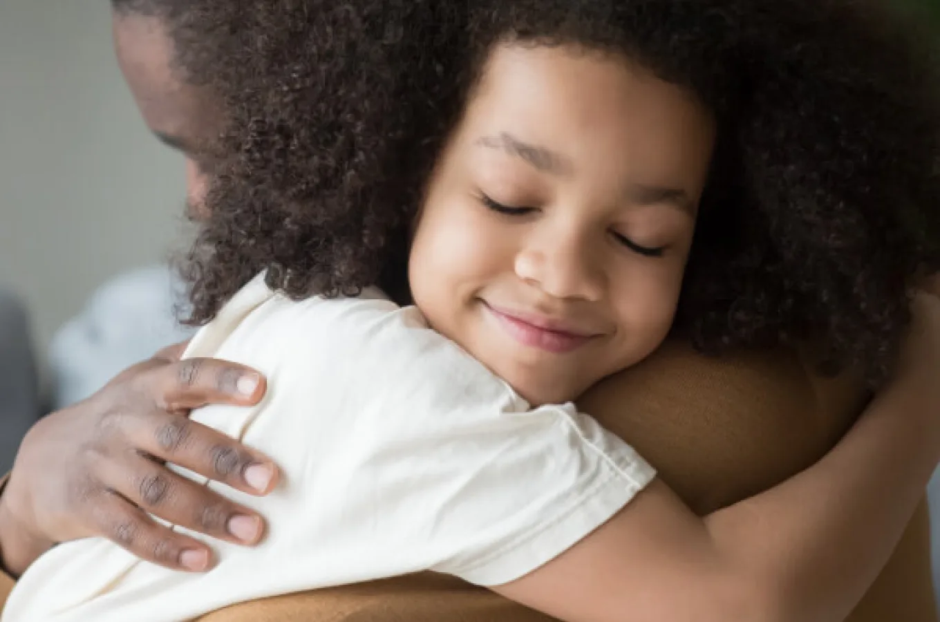 An adult embracing a young child, whose eyes are closed and whose cheek rests on the adult's shoulder