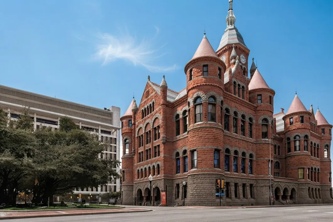 The historic Dallas County courthouse, a red sandstone building with pointed turrets and a clock tower against a blue sky.