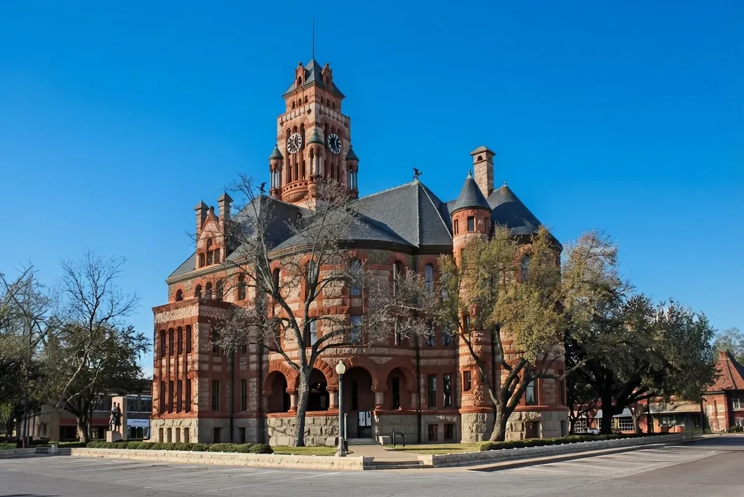 The Ellis County courthouse, a red stone building with a clock tower and dark roofs behind bare trees.