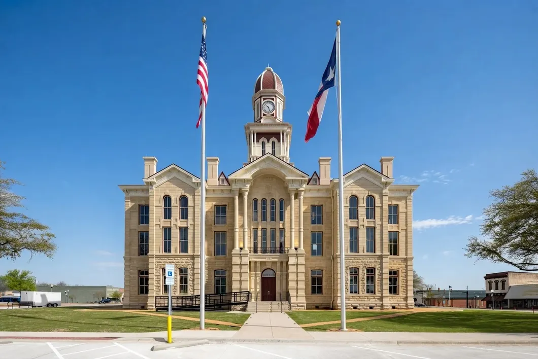 The Fannin County courthouse, a cream stone building with a small clock tower between two tall flagpoles.