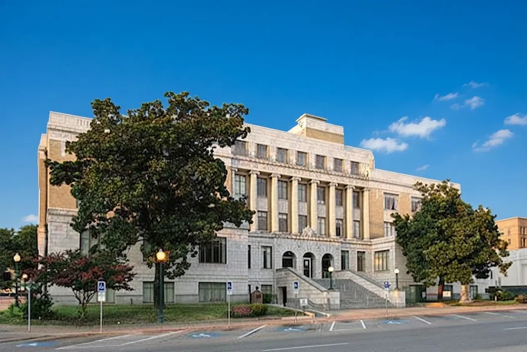 The Hunt County courthouse, a pale multi-story building with a stone entrance stair, shaded by large trees.
