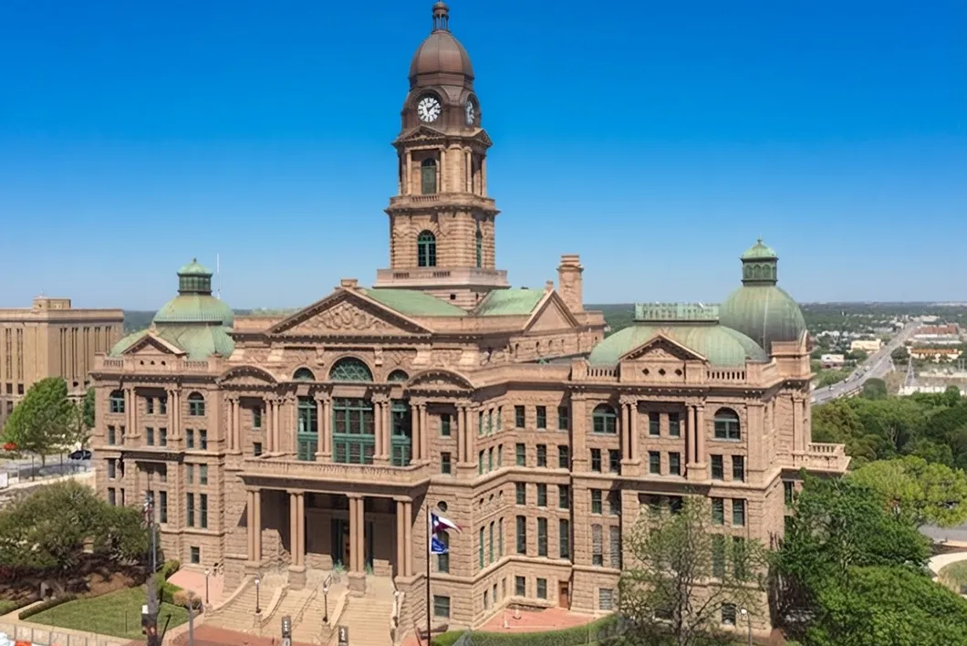 The Tarrant County courthouse, a pink granite building with a clock tower and green domes, seen from a raised angle.