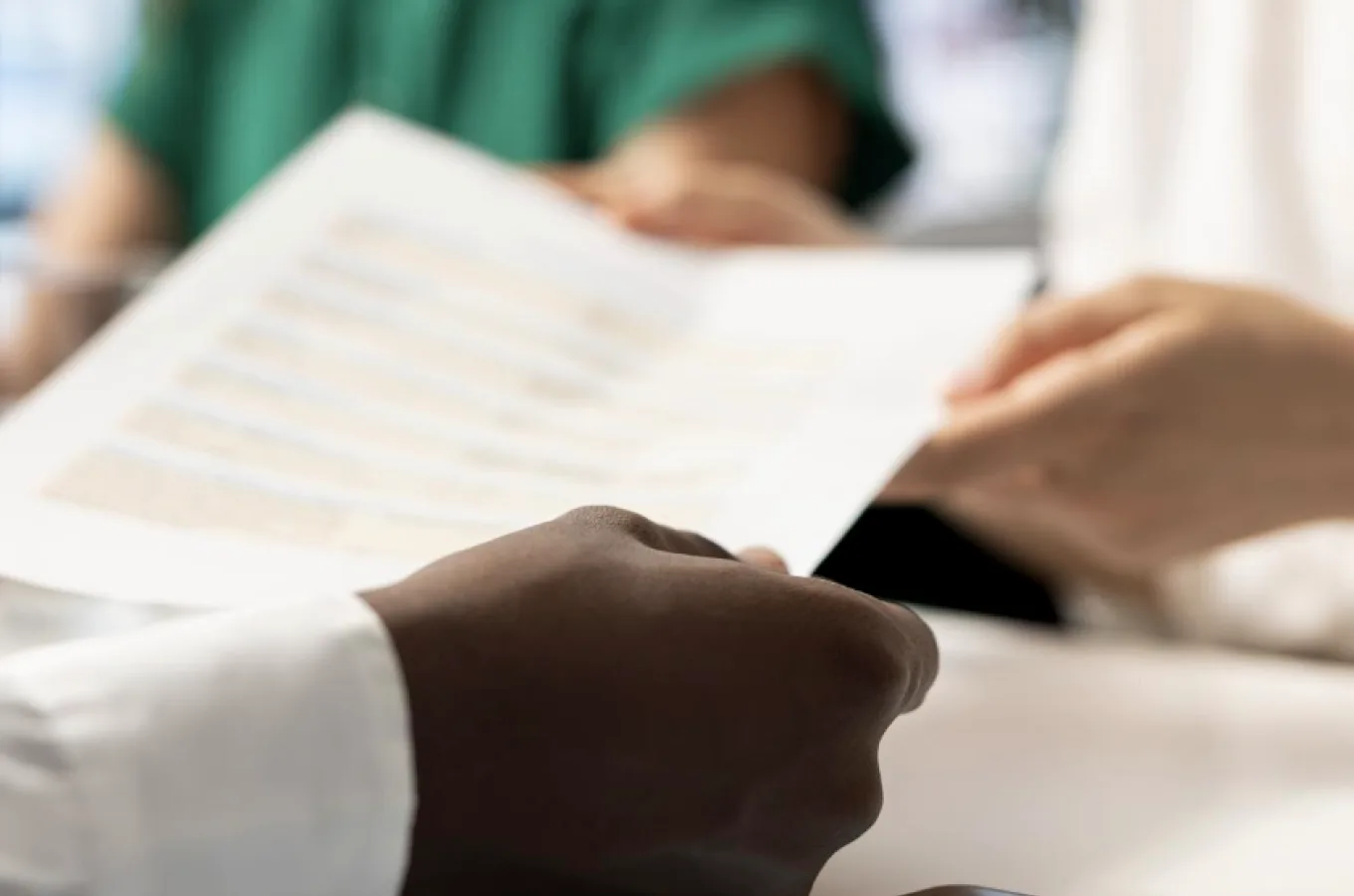 Close-up of two people at a table, one holding out a printed document toward the other's hands.