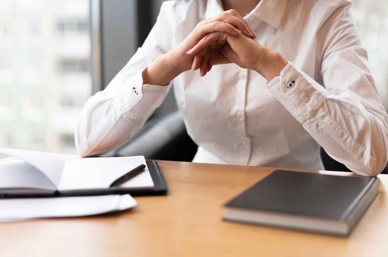 A person at a desk, hands clasped, with a notebook and closed books in front of them