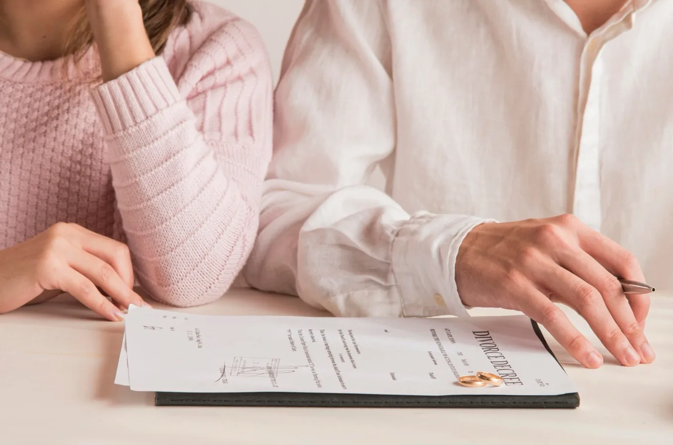 A couple's hands near a signed divorce decree, with two wedding rings set beside it