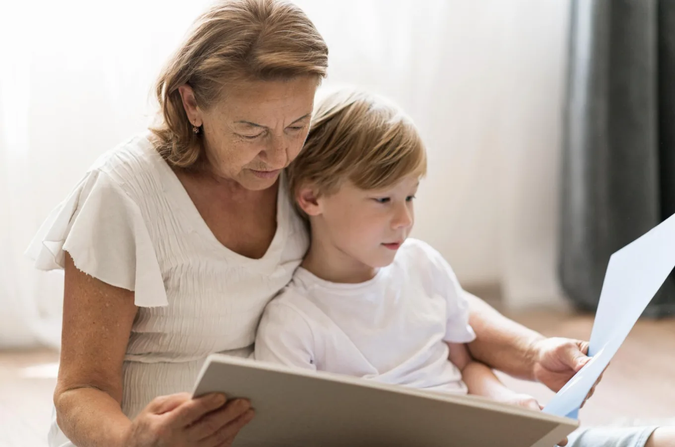 An older woman and a young boy sitting close together, looking at the open pages of a large book