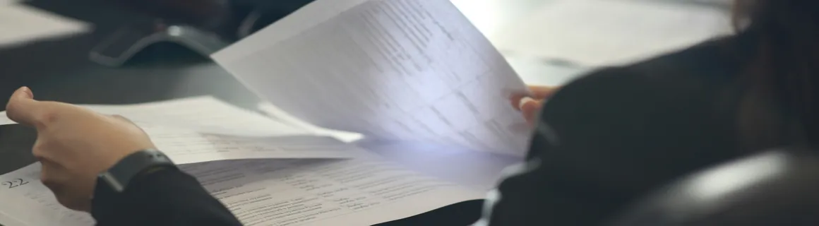 Two hands holding printed pages across a desk