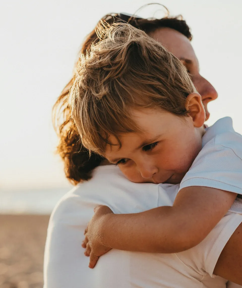 A young child resting on an adult's shoulder on a beach