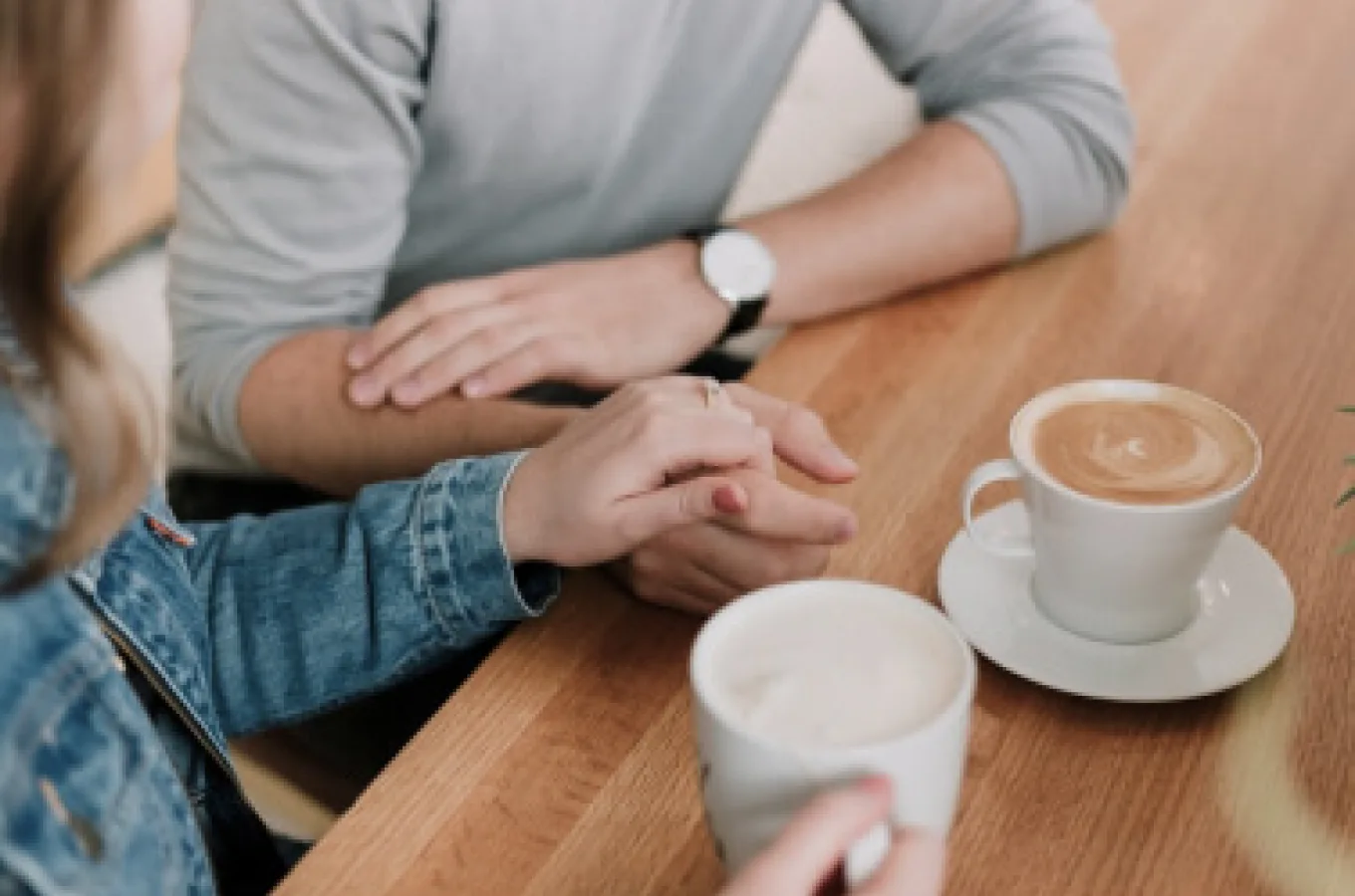 Two people's hands clasped together on a wooden table, next to two cups of coffee