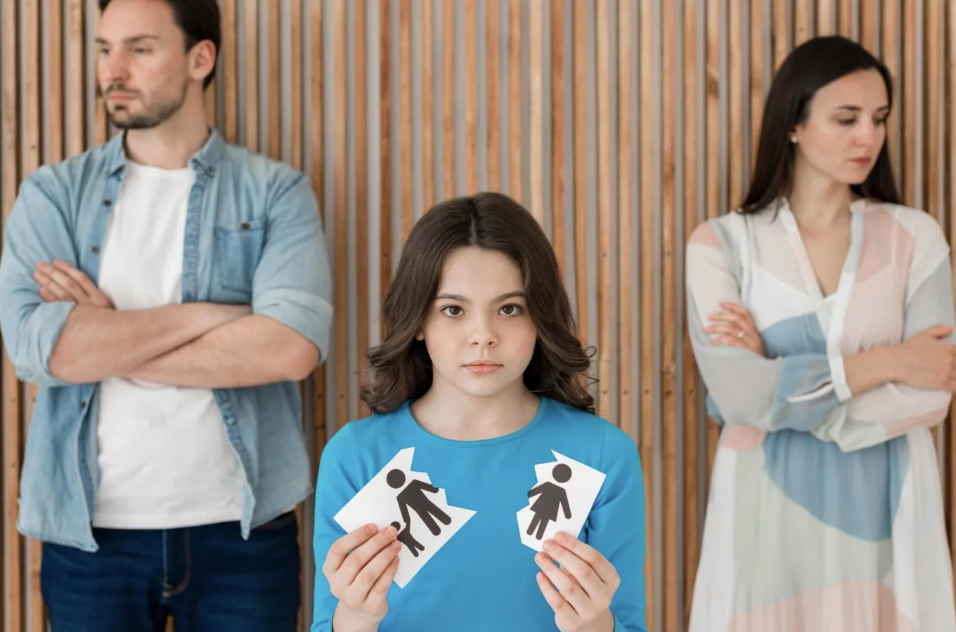 A child holding two torn halves of a paper cutout, standing between a man and a woman with folded arms