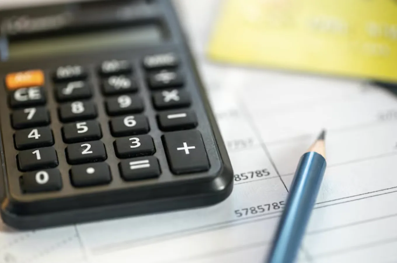 A calculator and a sharpened pencil resting on a printed statement, with a yellow card out of focus behind them.